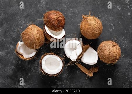 Coconuts cracked and whole on black background, top view Stock Photo