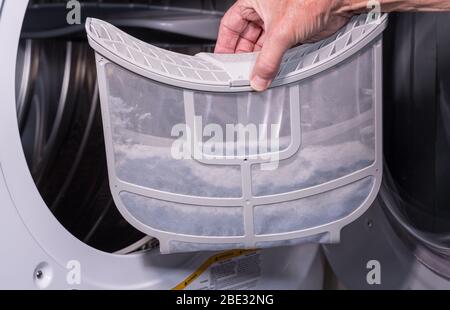 Senior caucasian man holding the lint filled trap from a front loading tumble dryer Stock Photo