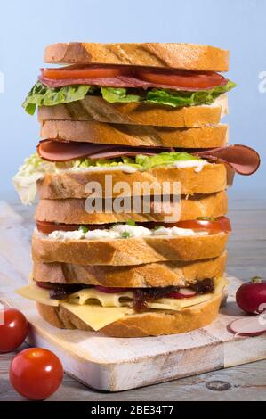 Tower of varieties of meat and vegetarian sandwiches on a rustic cutting board. Stock Photo
