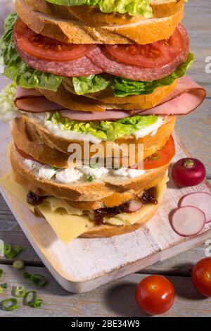 Tower of varieties of meat and vegetarian sandwiches on a rustic cutting board. Stock Photo