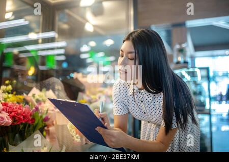 Dark-haired asian flower shop assistant making notes Stock Photo