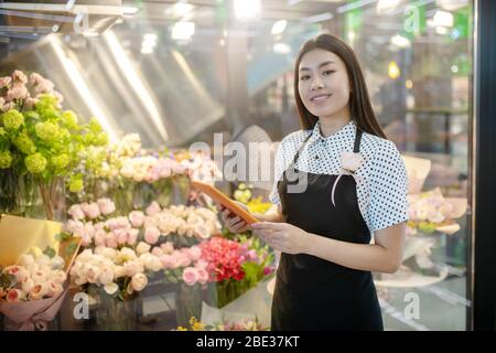 Dark-haired asian flower shop assistant looking thoughtful Stock Photo