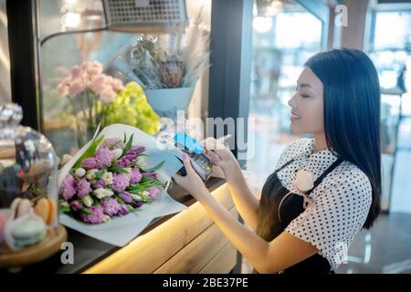 Dark-haired female flower shop assistant holding a credit card Stock Photo