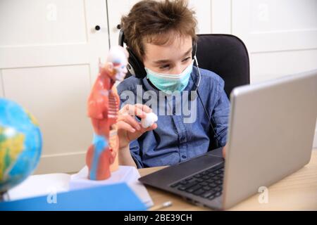 Distance learning online education. schoolboy in medical mask studying at home, coronavirus quarantine Stock Photo