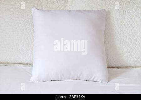 Square white throw pillow resting lazily against two beautiful quilted white pillows. Stock Photo