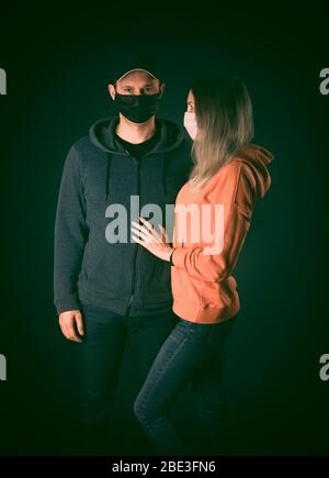 Fashion young adult man and woman in protective medical masks on black background night. Coronavirus victory concept and love Stock Photo