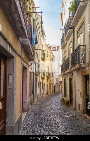 Old residential buildings along an empty, narrow and idyllic cobblestoned alley (Rua do Salvador) in the Alfama district in Lisbon, Portugal. Stock Photo