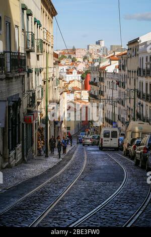 Old residential buildings, cars and few people on a hilly cobblestoned street (Calcada de Santo Andre) in the Alfama district in Lisbon, Portugal. Stock Photo