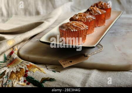 Home made fresh delicious cup cakes on white plate on marble top on canvas with gift tag with sign With Love. Green plant on background. Stock Photo