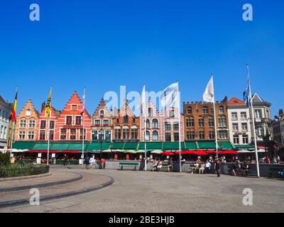 Typical colorful buildings in a pubblic square in Brugge, Belgium with flags under a blue sky Stock Photo