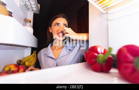 Woman closing nose near refrigerator, feeling bad smell Stock Photo