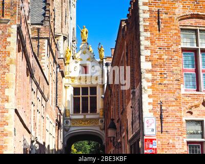 Close up of a white bridge connecting two typical Flemish buildings with golden statues and details in Brugge, Belgium Stock Photo