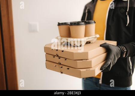 Close up of man hold tree boxes of pizza. Man delivery food and coffe to customer in mask and gloves. Coronavirus theme Stock Photo