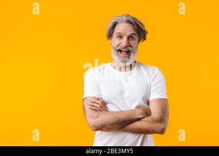 Image of cheerful positive senior grey-haired bearded man posing isolated over yellow wall background. Stock Photo