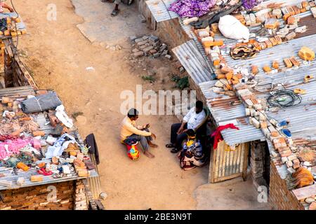 Aerial shot of people sitting wearing face masks outside their ramshakle temporary houses in a slum Stock Photo