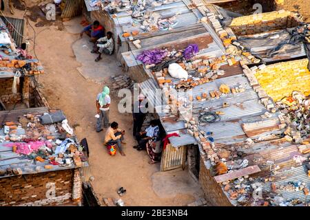 Aerial shot of people sitting wearing face masks outside their ramshakle temporary houses in a slum Stock Photo