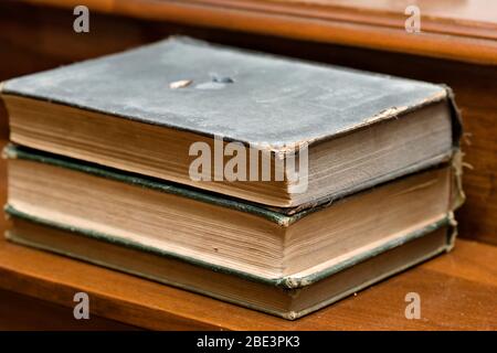 Three worn hardback books stacked horizontally on a wooden surface. Stock Photo