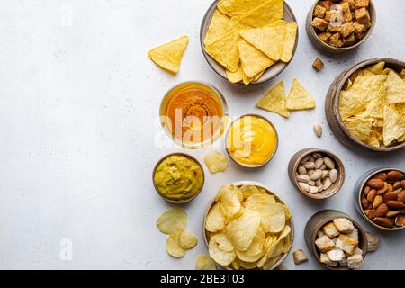 Veraity bowls of beer snacks and sauces on stone table. Nuts, chips, nachos, crackers. Top view with copyspace Stock Photo