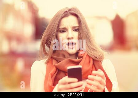 SMS. Closeup portrait funny shocked anxious scared young girl looking at phone seeing bad news photos message with disgusting emotion on face isolated Stock Photo