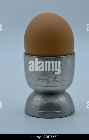 Isolated close-up silver or pewter egg cup with a tiki motif engraved on it and a boiled egg in it Stock Photo
