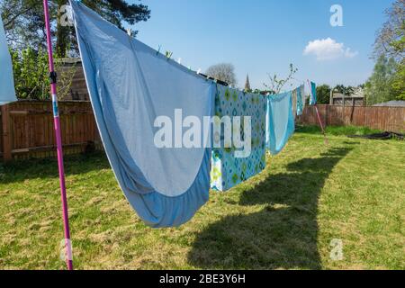 Bedding and sheets are freshly laundered and are hanging out to dry on a washing line in residential back garden. Stock Photo