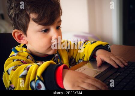 3 years old curious Turkish baby wearing yellow pajamas playing games with laptop Stock Photo