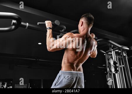 The athlete does a pull-up on the horizontal bar. A man in great shape is doing pull-ups on the horizontal bar from the entrance hall. Dark background Stock Photo