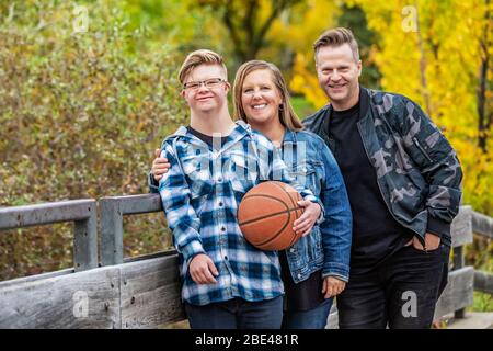 A young man with Down Syndrome with his father and mother while enjoying each other's company in a city park on a warm fall evening Stock Photo