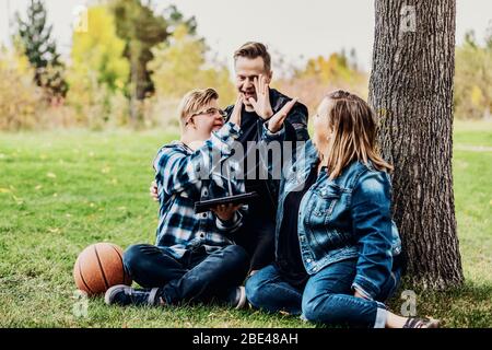 A young man with Down Syndrome celebrates with a high-5 after winning a game on his pad while enjoying quality time with his father and mother in a... Stock Photo