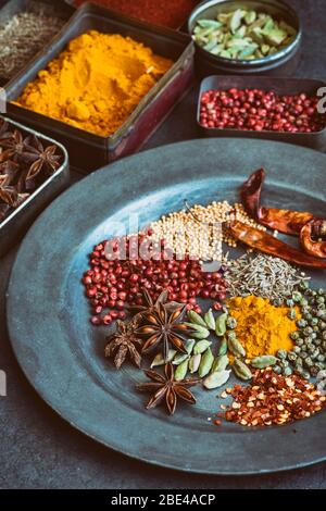 Aromatic spices in tins on and around a pewter plate on slate background Stock Photo