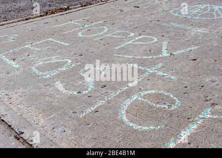 Writing on the sidewalk in colorful chalk reads "Hoppy Easter" amid some drawings laid out in the neighborhood for the spring holiday. Stock Photo