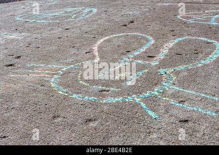 A drawing of a smiling bunny's face in colorful chalk appears on a concrete sidewalk during the Easter season. Stock Photo