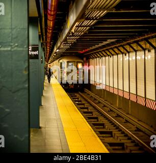 Underground subway on tracks with people walking on platform; New York City, New York, United States of America