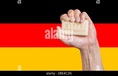 Caucasian male hand holding a bar of soap with words: Bitte Hande Waschen against a German flag background