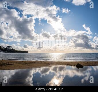 Sun shining through clouds and reflecting in the low tide sea water on the beach Stock Photo