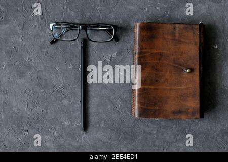 Brown craft leather notebook, pen and glasses on gray background. Stock Photo