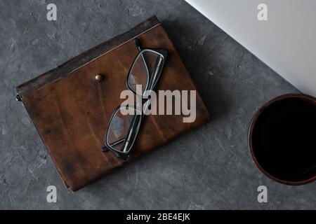 Brown leather notebook, pen, laptop and glasses on gray background. Stock Photo