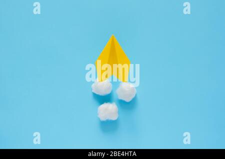Yellow paper airplane moving on the clouds with blue background. Minimal travel and vacation concept. Stock Photo