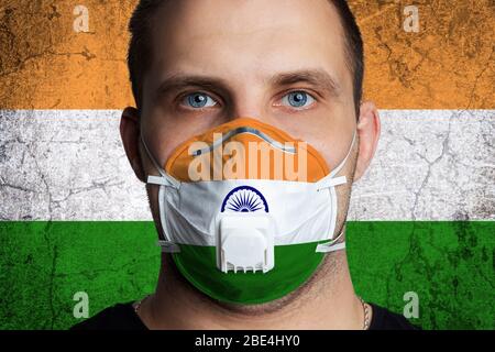 Young man with sore eyes in a medical mask painted in the colors of the national flag of India. Coronovirus disease  COVID-19 concept.  Man is afraid Stock Photo