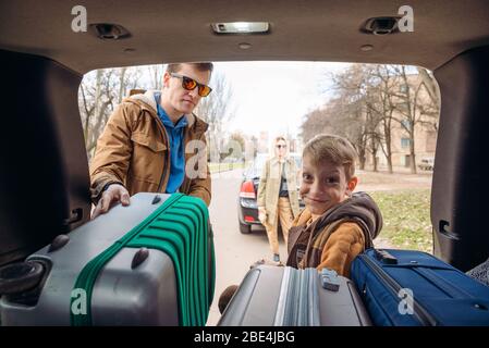 family with kid putting bag in car trunk Stock Photo
