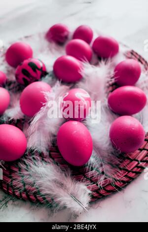 Top view of pink chicken easter eggs, white feathers, brushes, paints on marble background. Preparation for coloring eggs at Easter. Creative process Stock Photo
