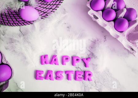 Creative bright composition with festive atmosphere. Easter holiday decorations on marble background. Fluffy white feathers and painted purple eggs in Stock Photo