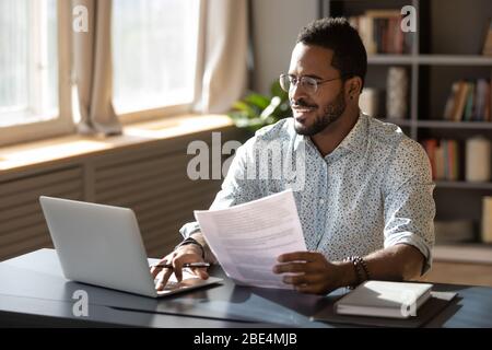 Happy millennial african american businessman in eyewear doing paperwork. Stock Photo