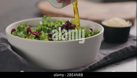 pour olive oil over dried cranberries with kale in white bowl on kitchen countertop Stock Photo
