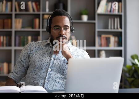 Focused millennial mixed race guy consulting clients online. Stock Photo