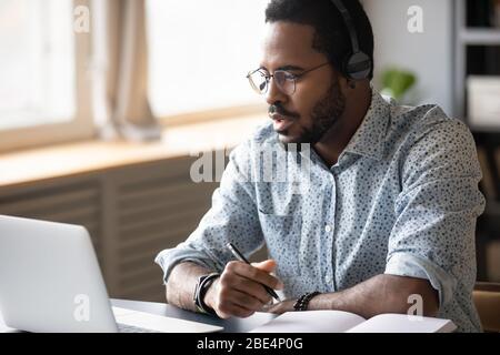 Focused young african american man watching educational lecture online. Stock Photo