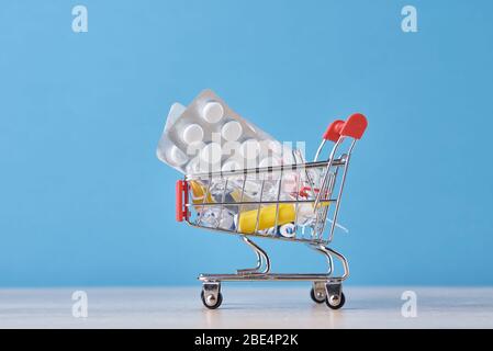 Shopping trolley cart with medicine pills on blue background. Health care and medicine concept Stock Photo