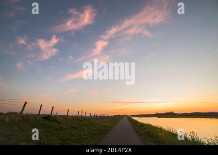 Path along a river is vanishing in the distance. Beautiful colors of the clouds just after sunset. Stock Photo
