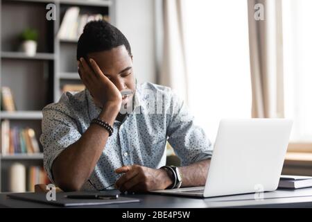Tired young african man leaning on hand, sleeping at table. Stock Photo