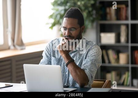 Smiling handsome young african american guy looking at computer screen. Stock Photo